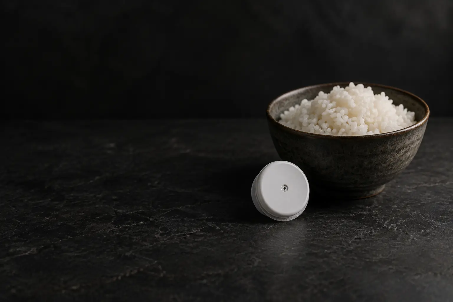 A small round white continuous glucose monitor sensor resting beside a small bowl of cooked white rice